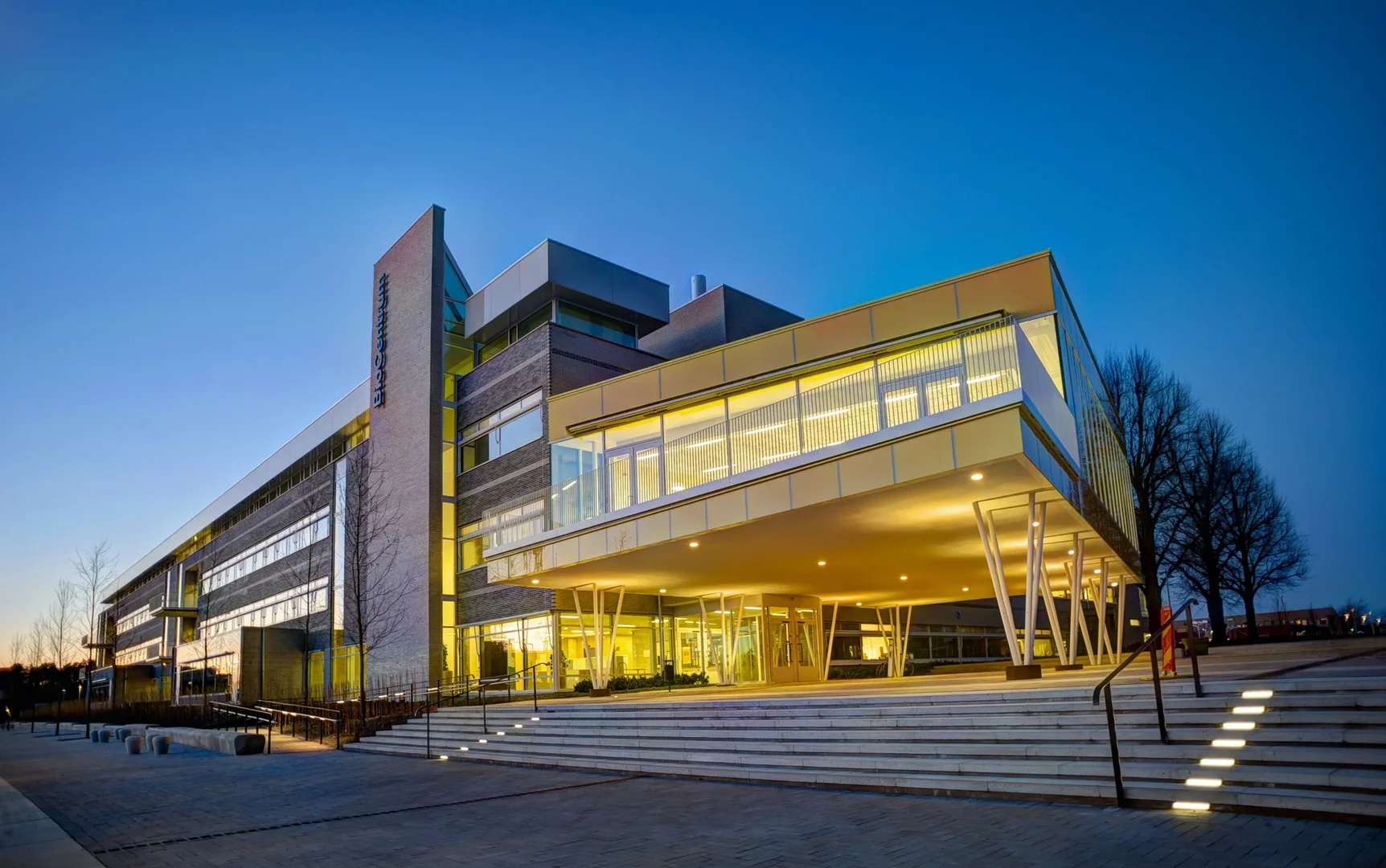 Eine Wissenschaftlerin und ein Wissenschaftler arbeiten hinter einer Glasfassade und mischen Chemikalien mit Großgeräten.