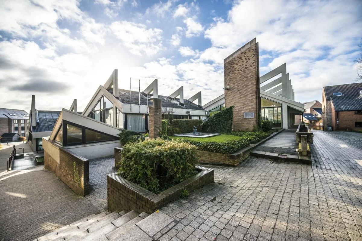 Eine Wissenschaftlerin und ein Wissenschaftler arbeiten hinter einer Glasfassade und mischen Chemikalien mit Großgeräten.